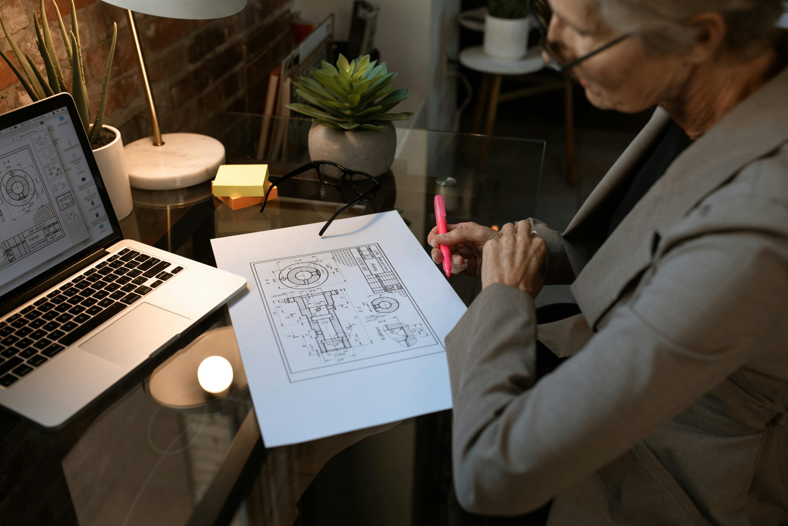 Contract Drafting Review and Para Legal Senior woman analyzing architectural plans with laptop in modern workspace.