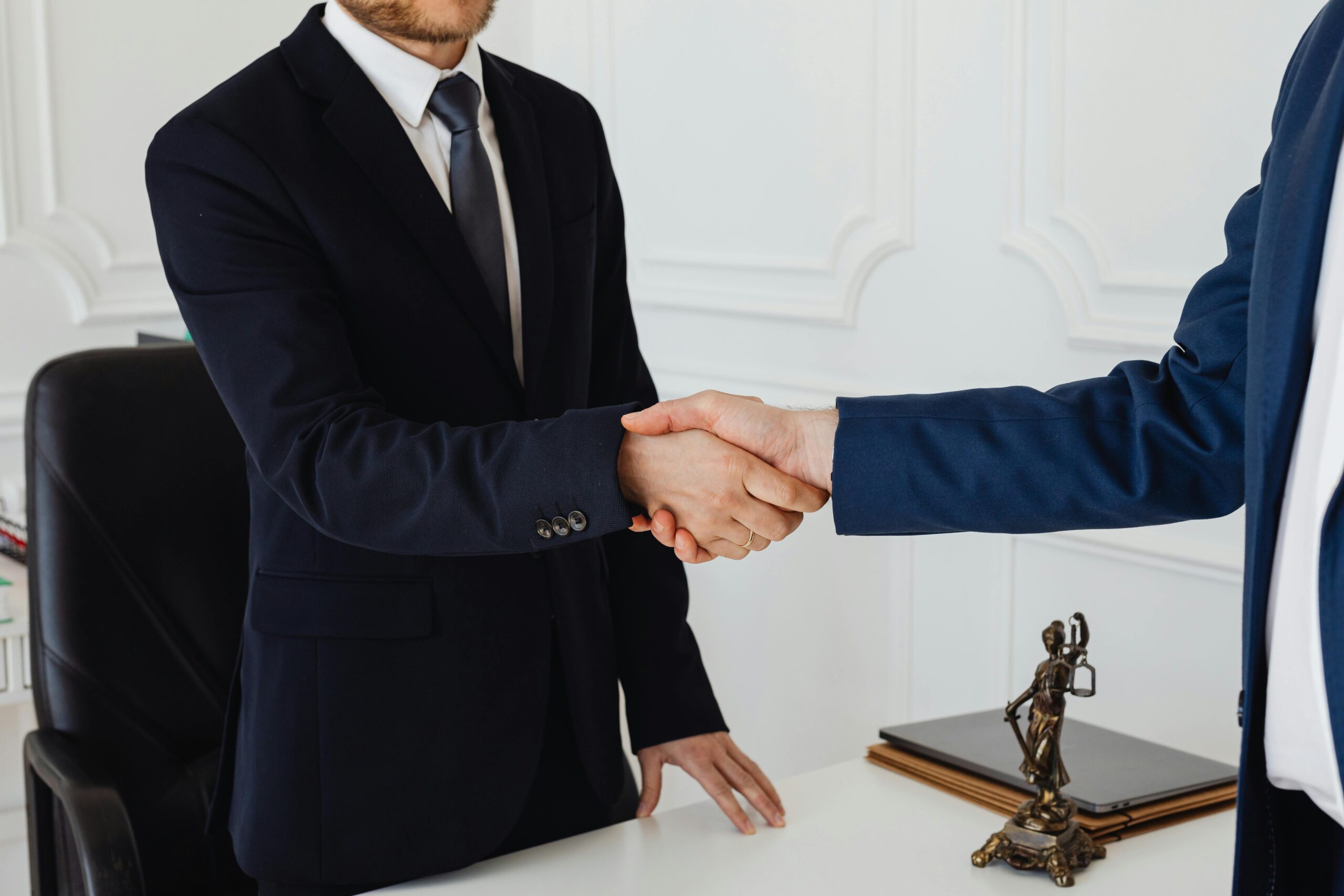 Rera Advocate Two men in suits shaking hands in a formal office environment symbolizing an agreement.