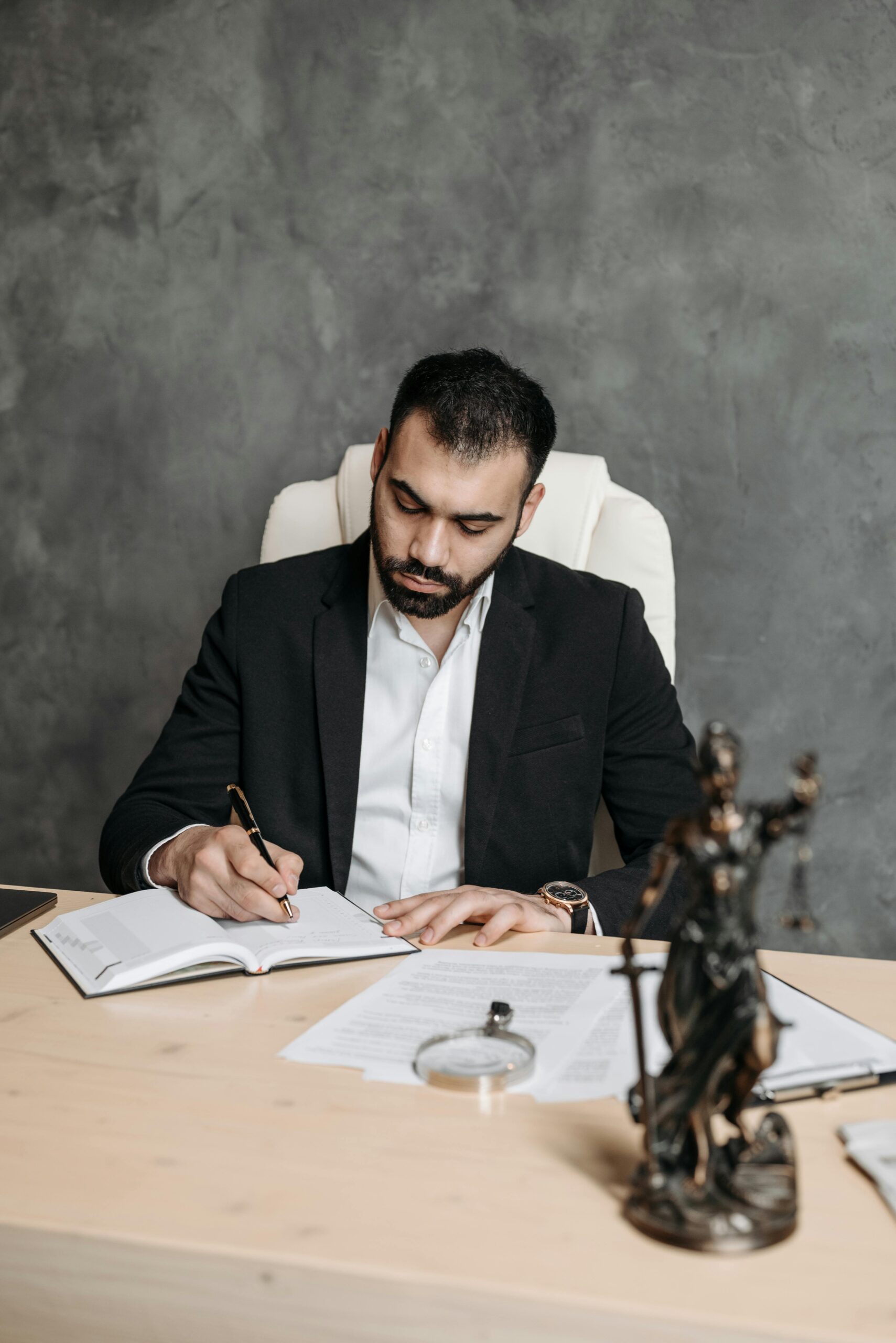 Contract Drafting Review and Para Legal Professional lawyer in a suit taking notes at a desk with legal documents and statue.